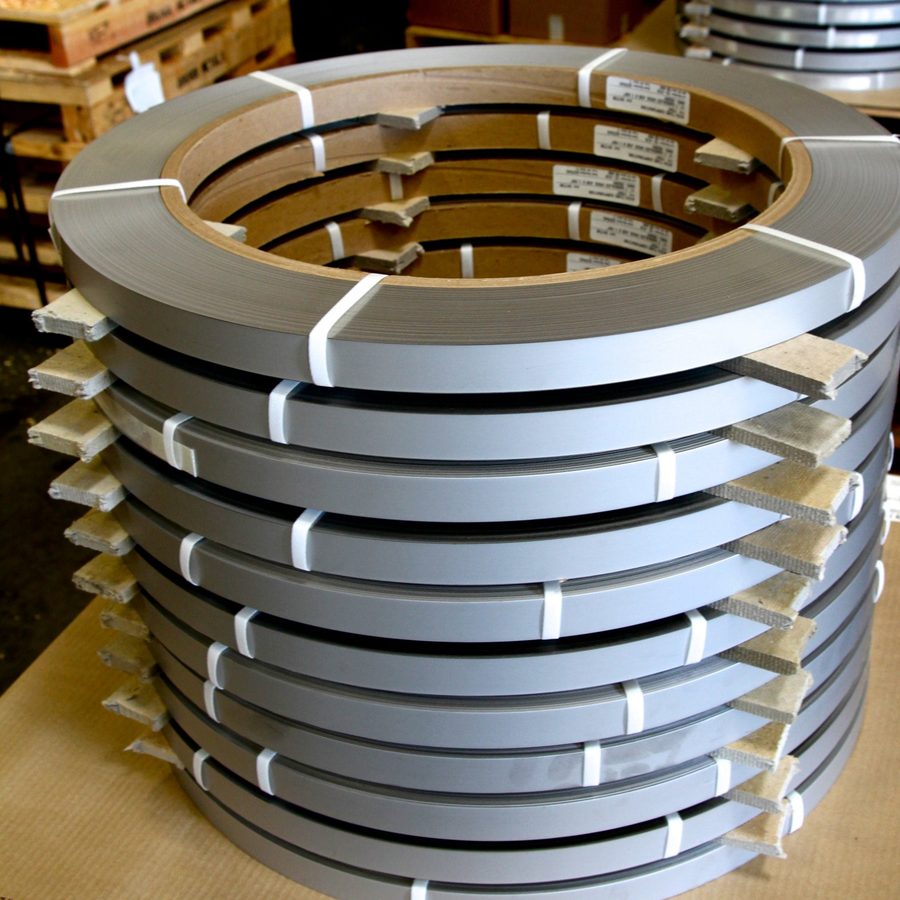 A stack of narrow stainless pancake coils on cardboard cores, separated by spacers and strapped for shipping.