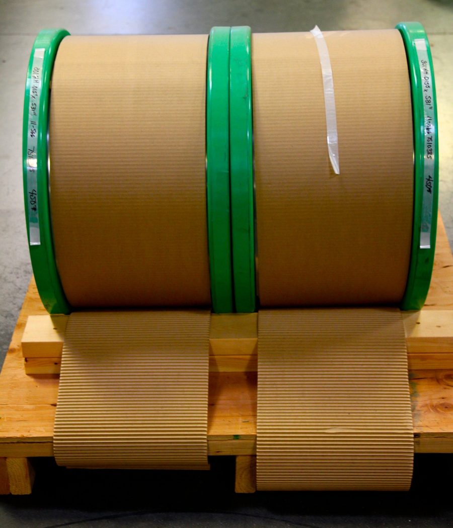 Two wound spools on a wooden skid, wrapped in corrugated cardboard for shipping.